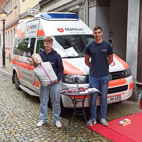 Zwei junge Männer stehen vor einem Krankenwagen.