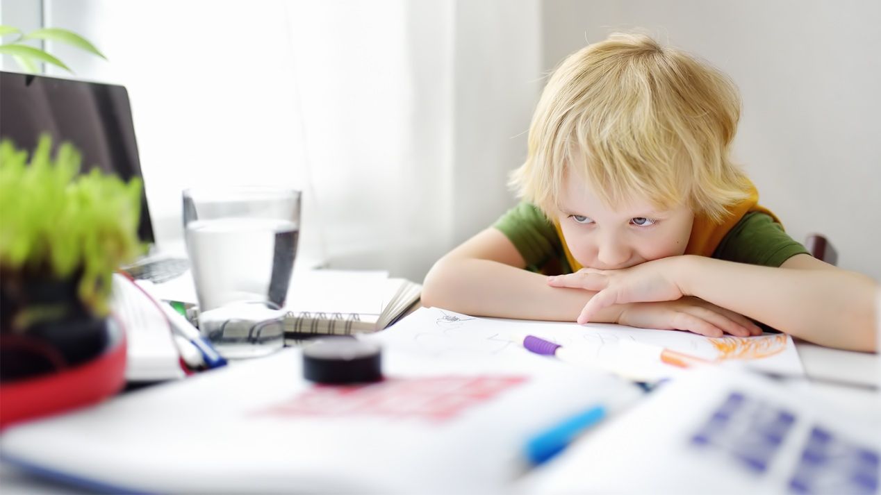 Ein kleiner Junge sitzt mit unglücklichem Gesichtsausdruck an einem Tisch.