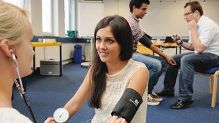 Bei einem Erste-Hilfe-Kurs wird einer jungen Frau der Blutdruck gemessen.