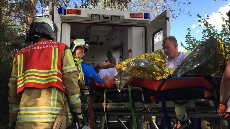 Rettungskräfte kümmern sich um einen Mann, der auf einer Fahrtrage vor einem Rettungswagen liegt.