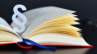 Ein aufgeschlagenes Buch mit einem Paragrafenzeichen zwischen den Seiten.