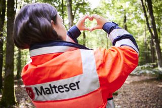 Malteser Helferin formt mit den Händen ein Herz.