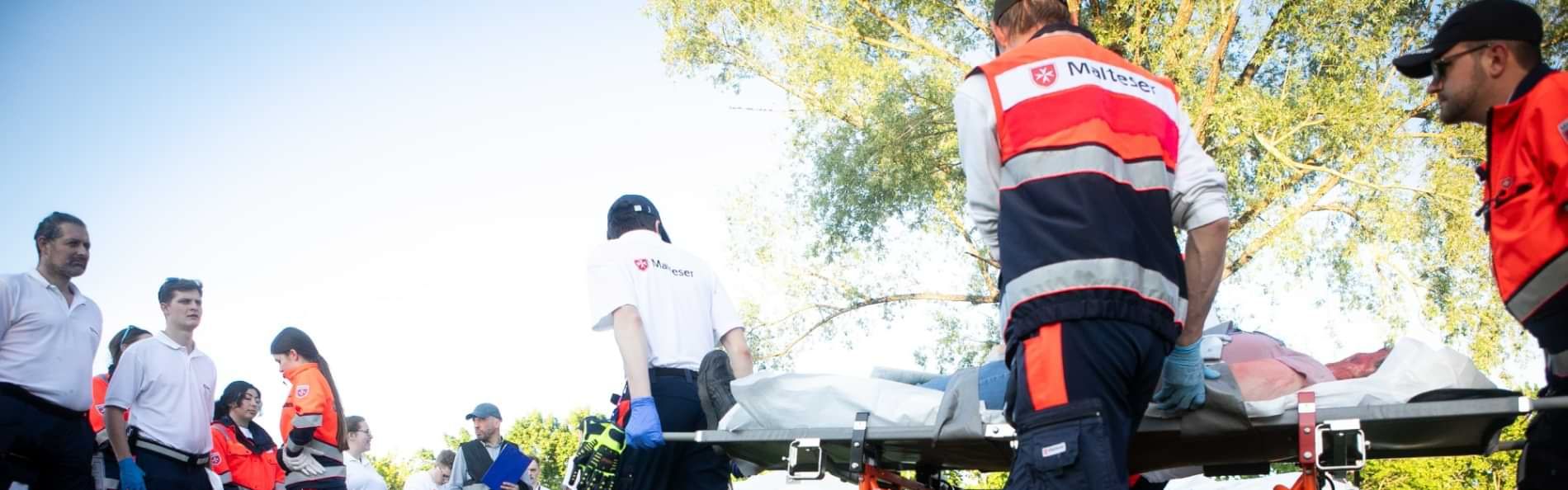 Menschen in Einsatzkleidung der Malteser bei einer Übung auf einer Wiese.