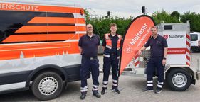 Drei Männer stehen vor einem Fahrzeug des Katastrophenschutzes und einem Tankanhänger der Malteser