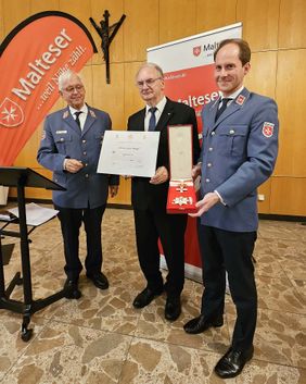 Drei Männer posieren bei der Ordensverleihung, Dr. Reiner Haseloff hält eine Urkunde, Stefan Gäbler das Ehrenkreuz-Etui.