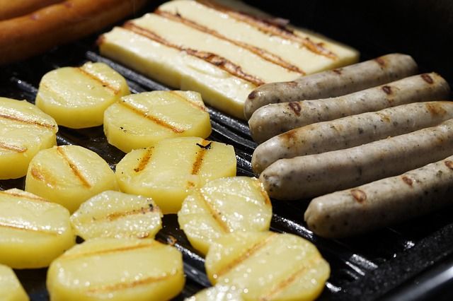 Kartoffelscheiben, Bratwürste und Grillkäse auf einem Grillrost
