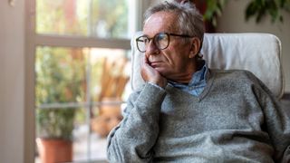 Älterer Mann mit gelangweiltem Gesichtsausdruck schaut aus einem Fenster.