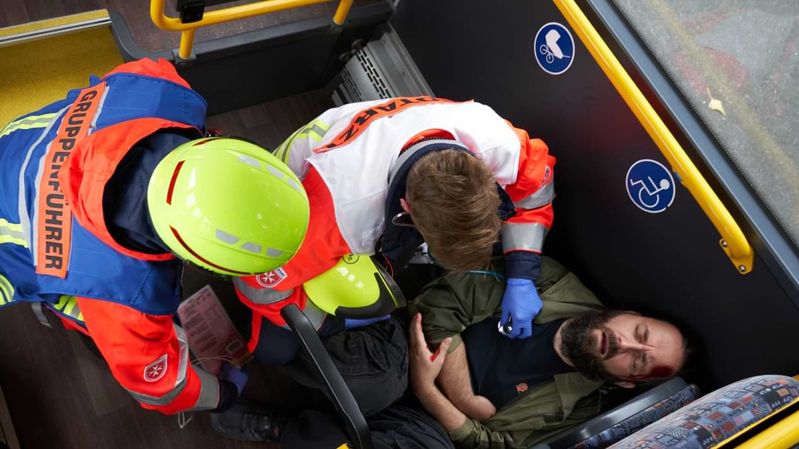 Ein Verletzter in einem Linienbus wird von zwei Helfern versorgt.