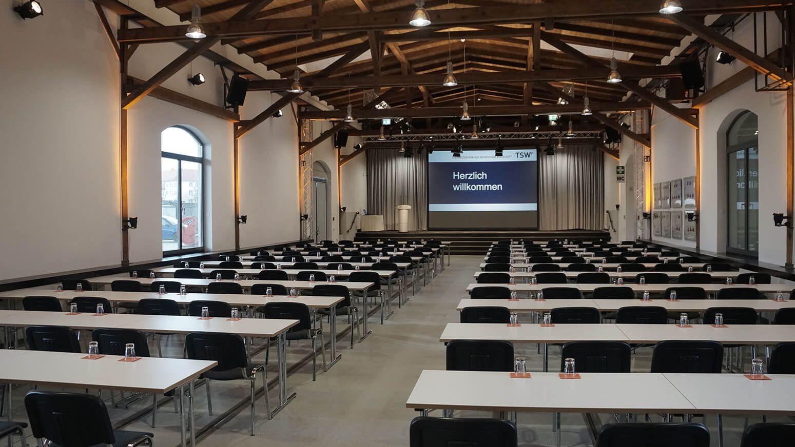 Großer Veranstaltungssaal im Tagungszentrum mit Reihenbestuhlung, Bühne und Präsentationsleinwand.