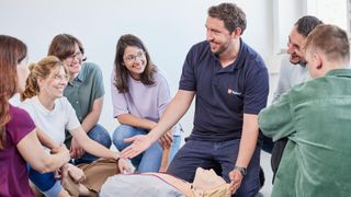 Erste-Hilfe-Ausbilder der Malteser steht vor einer Gruppe in einem Erste-Hilfe-Kurs