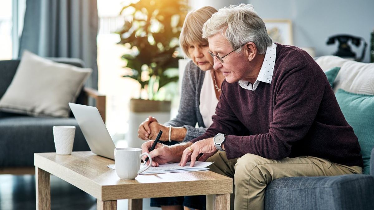 Ein älteres Paar mit Laptop und Papieren im Wohnzimmer