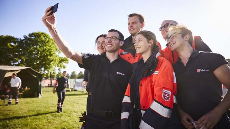 Eine Gruppe junger Menschen. Einer von ihnen hält ein Smartphone, um ein Selfie zu machen.