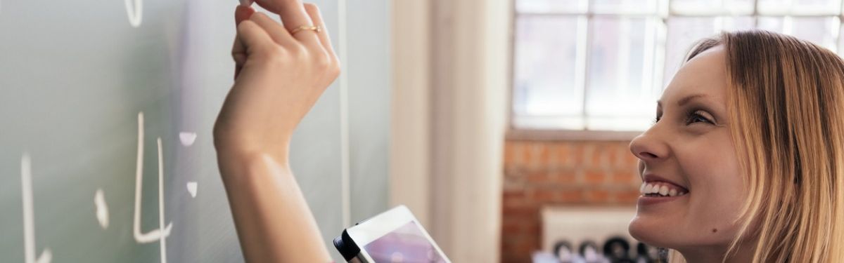 Junge Frau mit Tablet schreibt etwas an eine Tafel.