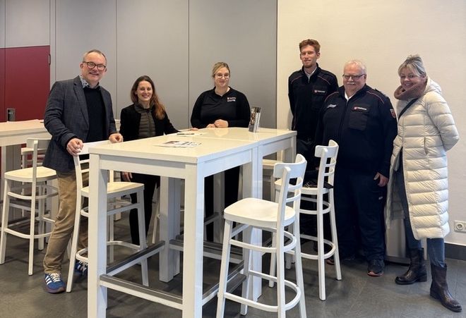 Sechs Personen stehen um einen Stehtisch herum und blicken in die Kamera