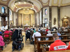 Sitzende Menschen in einer Kirche. Einige Personen mit Malteser Dienstbekleidung