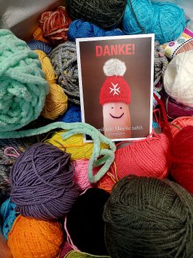 Eine Dankeskarte, die einen Finger mit Malteser Mützchen zeigt, inmitten von Wollknäulen (Quelle: Malteser)