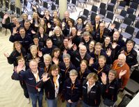 Größere Gruppe von Helferinnen und Helfern in Malteser Dienstbekleidung, die in die Kamera winken.