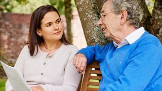 Eine jüngere Frau und ein älterer Mann sitzen im Garten auf einer Bank und sprechen über die Malteser Betreuungsverfügung