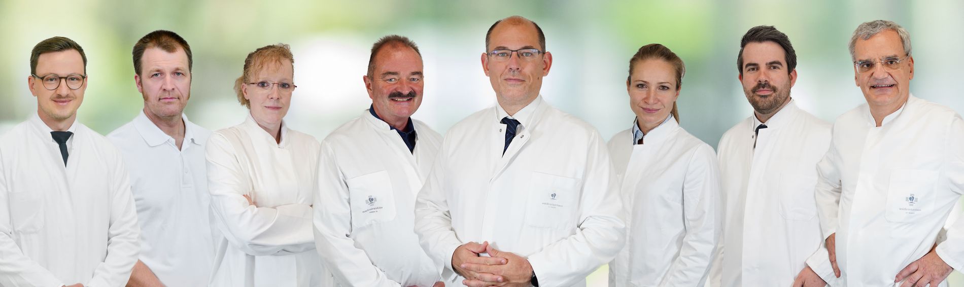 Acht medizinische Fachkräfte der Klinik für Orthopädie und Unfallchirurgie in weißen Kitteln stehen nebeneinander.