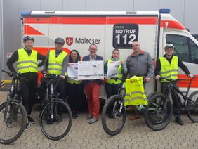 Gruppenfoto der Gewinner mit Fahrrad vor einem Krankenwagen