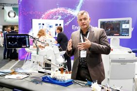 Mann zeigt auf Medizintechnik an einem Messestand mit Monitoren und Modellen vor Hintergrund mit der Aufschrift „Engineering“.
