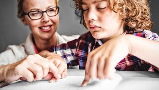 Frau sitzt hinter einem Jungen, der in Blindenschrift liest.