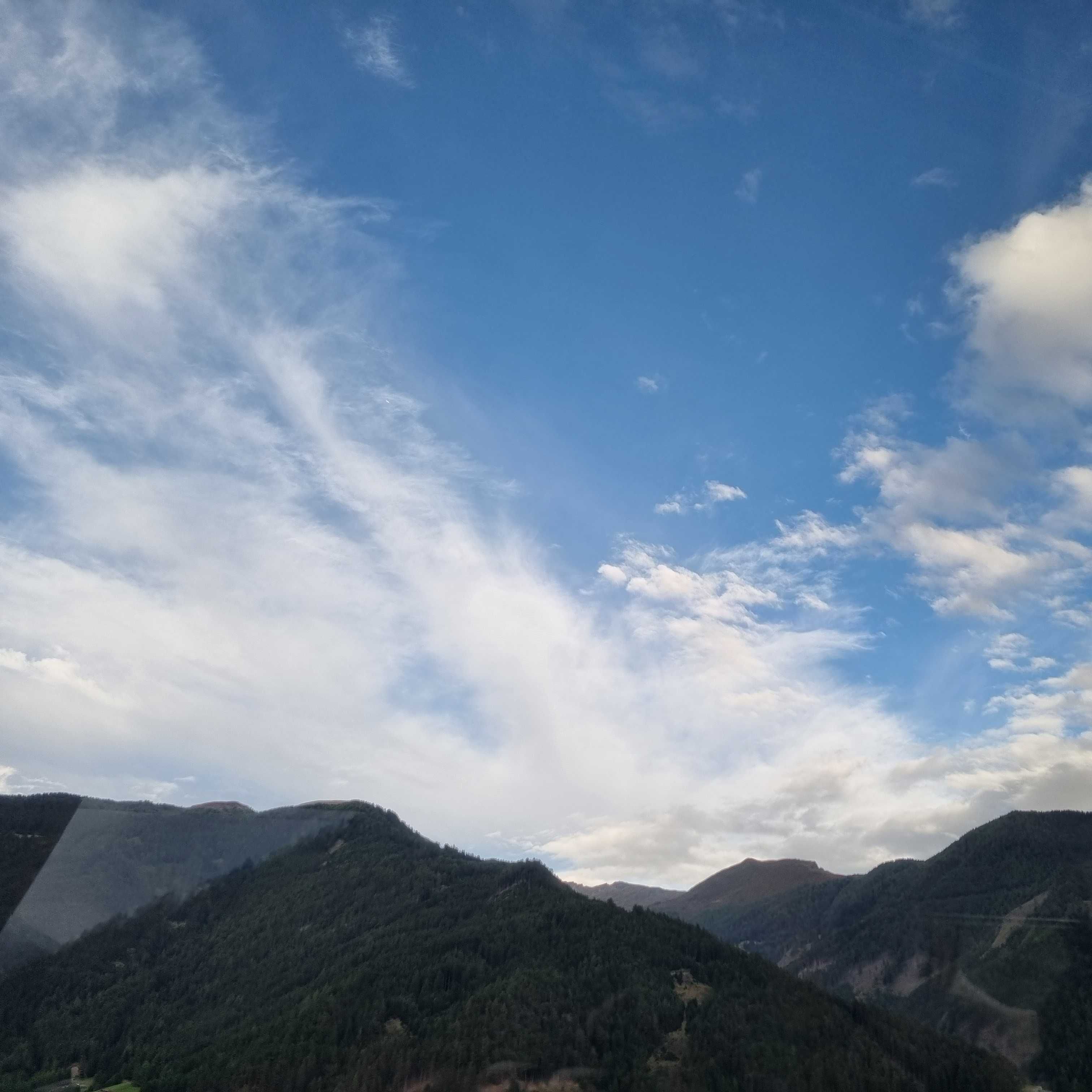 Berglandschaft mit bewaldeten Hügeln unter blauem Himmel mit weißen Wolken.