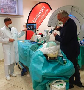 Arzt demonstriert einem Besucher an einem Modellkopf den Einsatz eines OP-Roboters mit Monitoranzeige.