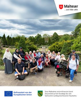 Eine größere Gruppe von Personen sitzt und steht gemeinsam in einem gepflegten Garten mit Wegen, Beeten und hohen Sträuchern unter einem bewölkten Himmel. Im Vordergrund sind einige Rollatoren zu sehen, während oben rechts das Malteser-Logo und unten Hinweise zur Förderung durch die Europäische Union eingeblendet sind.