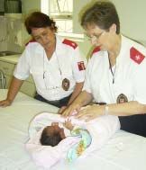 Two care workers tending to a newborn on a cot.
