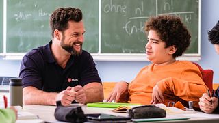 Malteser Schulbegleiter sitzt mit einem Jugendlichen im Rollstuhl im Klassenraum.