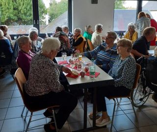 Ältere Menschen sitzen an mehreren Tischen