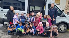 viele Kinder mit einigen Paketen stehen und knien vor einem offenen Malteser Kleinbus, daneben Schulrektorin Birneder und Malteser Kreisgeschäftsführer Bucher