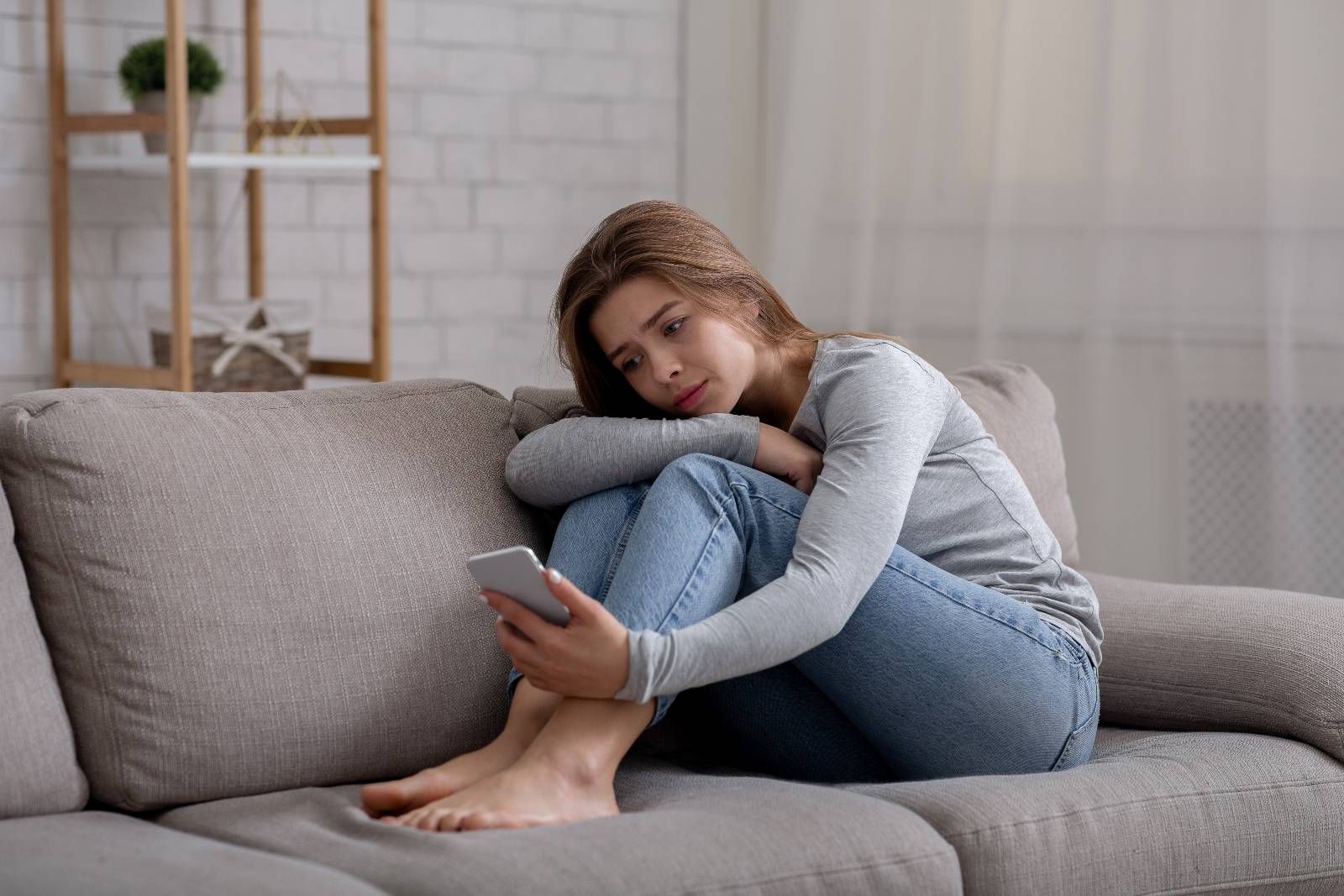 Traurige Frau sitzt auf dem Sofa und schaut auf Ihr Smartphone