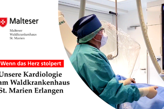 Kardiologe im OP-Saal blickt mit Haube und Maske auf Monitor.
