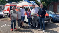 Eine Gruppe von Menschen steht vor einem Krankentransportwagen.