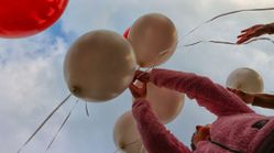 Mehrere goldene und ein roter Luftballon, die von Händen in einem rosa Pullover in den Himmel gelassen werden.