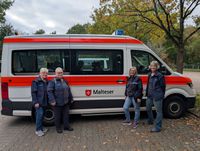 Die vier ehrenamtlichen Helferinnen des Kulturbegleitdienstes der Malteser Nordhorn posieren für ein Foto vor dem weiß-orangen Einsatzfahrzeug, das für die Touren verwendet wird.