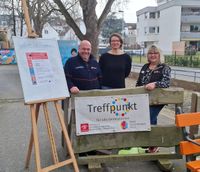 Ein Malteser-Ehrenamtler steht mit zwei Kooperationspartnerinnen im Freien an einem Schild mit dem Titel "Treffpunkt"