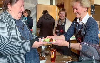 Eine Frau schenkt einer anderen Frau eine warme Mahlzeit aus.