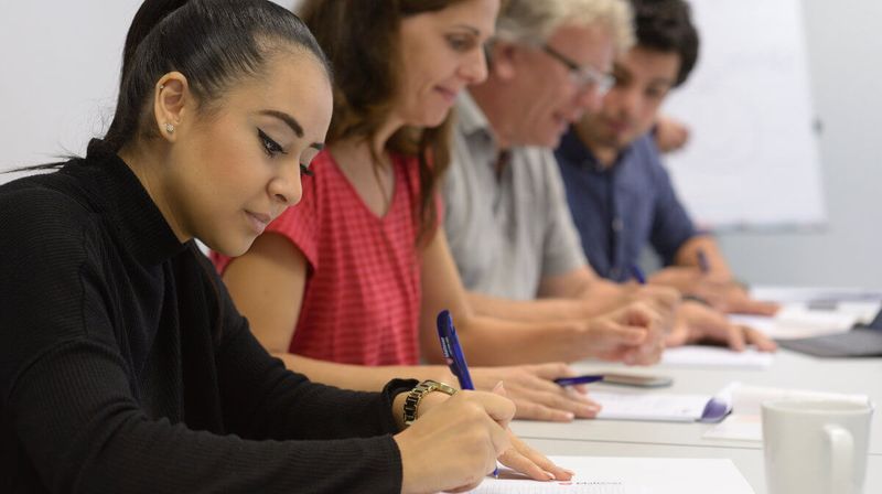 Menschen unterschiedlichen Alters schreibend an einem Tisch