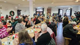 Menschen in einem Saal, der weihnachtlich geschmückt ist.