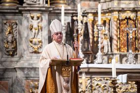 Ein Mann steht hinter einem Pult. Er trägt Kleidung, die in einer Kirche üblich sind.