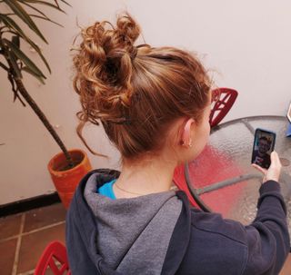 Eine junge Frau sitzt an einem Tisch mit ihrem Smartphone in der Hand. Sie führt einen Videocall mit einem jungen Mann, der Deutsch lernt.