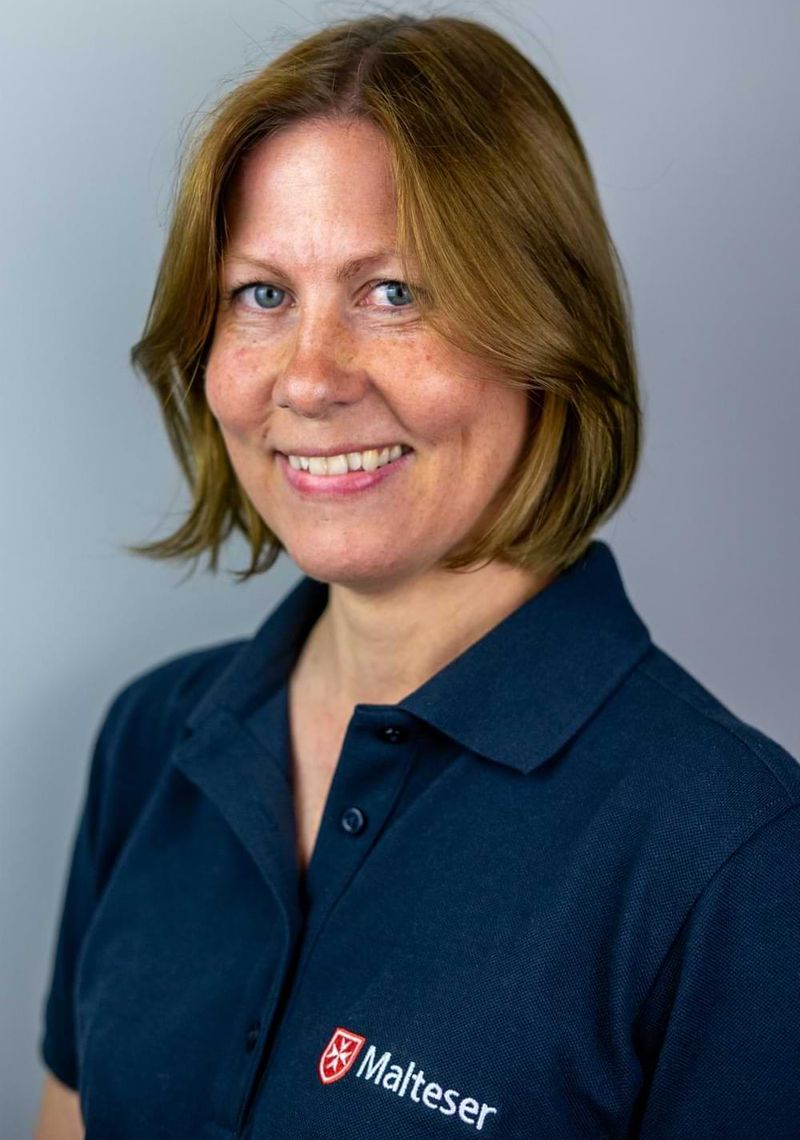 Portraitaufnahme einer lächelnden Frau in einem dunkelblauen Polohemd der Malteser. 