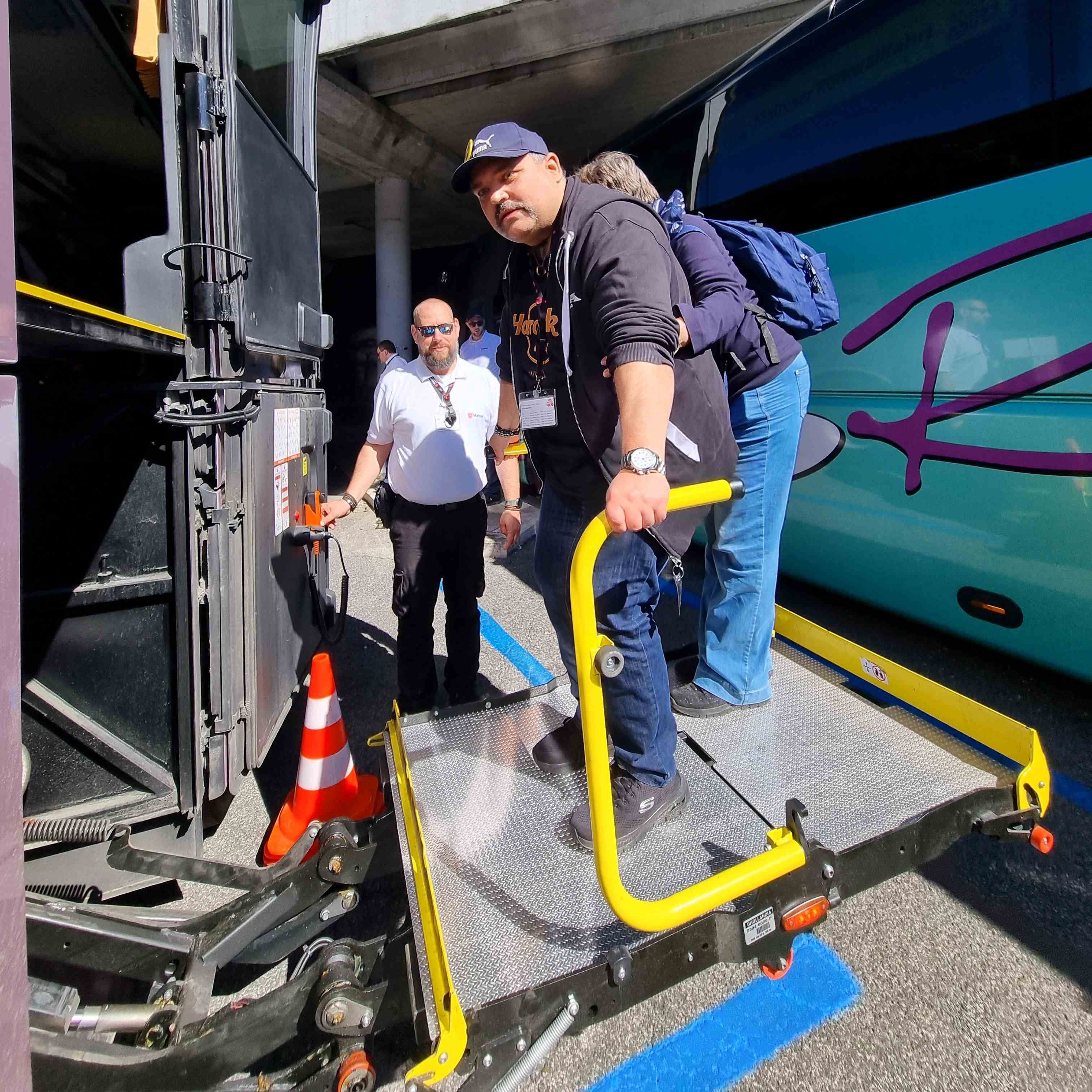 Mann mit Kappe und Rucksack steht auf Rampe eines behindertengerechten Busses, weitere Personen im Hintergrund.