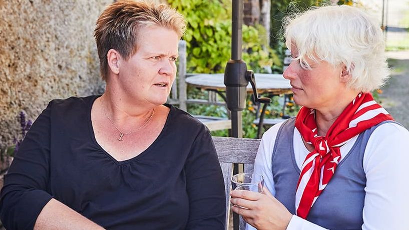 Zwei Frauen sitzen im Garten im Tisch und führen ein Gespräch. 