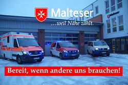 Drei Malteser Einsatzfahrzeuge mit Blaulicht vor Fahrzeughalle 