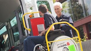 Malteser Mitarbeiter hilft einem Jungen im Rollstuhl ins Fahrzeug.