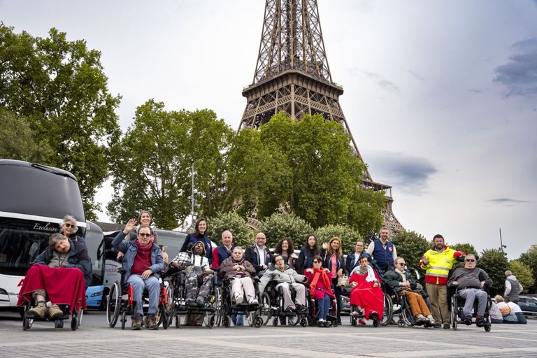 Eine Gruppe von Menschen, ein Teil davon in Rollstühlen, vor dem Pariser Eiffelturm